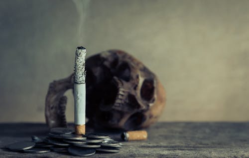Cigarette Stick on Pile of Coins