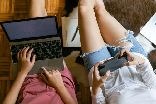 Crop women using gadgets on floor at home