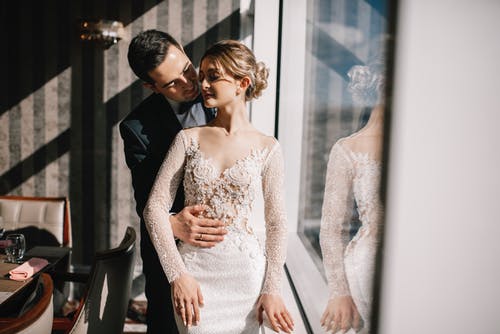 Woman in White Lace Dress Standing Beside Man in Black Suit