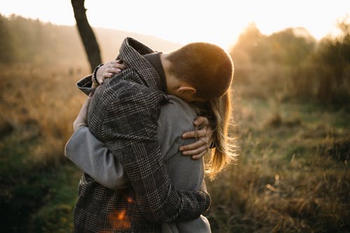 Man and Woman Standing and Hugging on Green Field