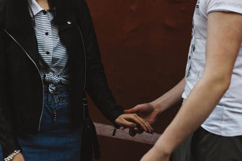 Standing Man in White Shirt Holding Hand of Woman in Black Jacket